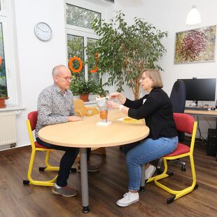 Treatment room with table and chairs and a computer workstation. You can see a treatment situation where the speech therapist is explaining something to the patient using a model.